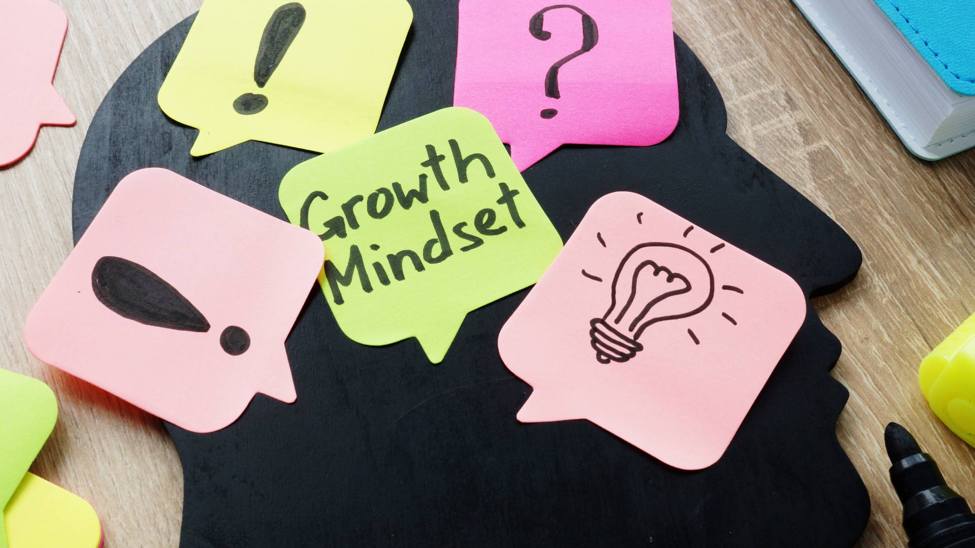 An image of post-it notes, one says growth mindset, and others have a picture of a lightbulb, question mark, and exclamation points. This photo emphasizes the differences between a growth mindset vs fixed mindset.