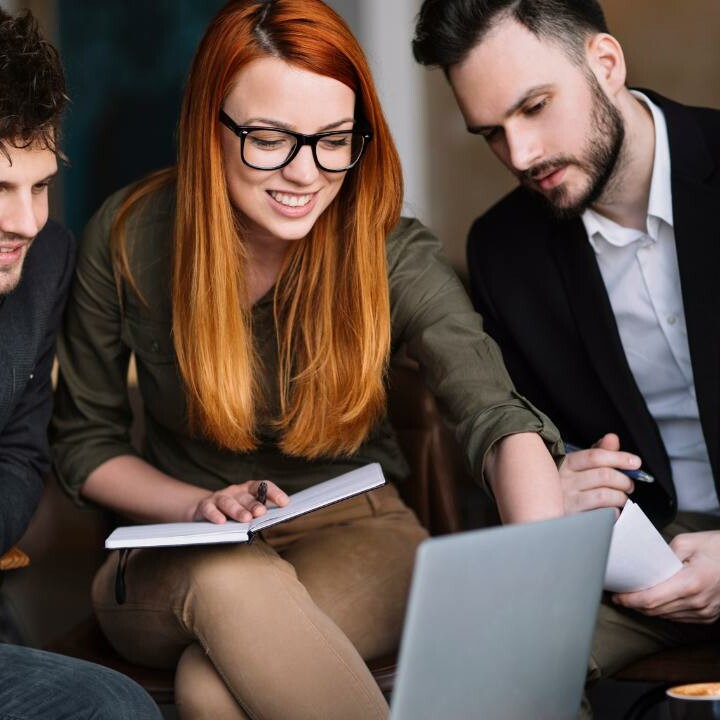 An administrative assistant thinking strategically and setting defined goals with a group of coworkers gathered around her computer.