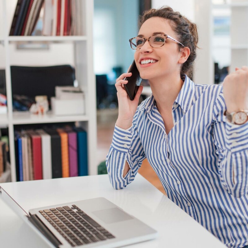 A successful administrative assistant sits at her desk on the phone, preparing for a career move to an executive assistant.