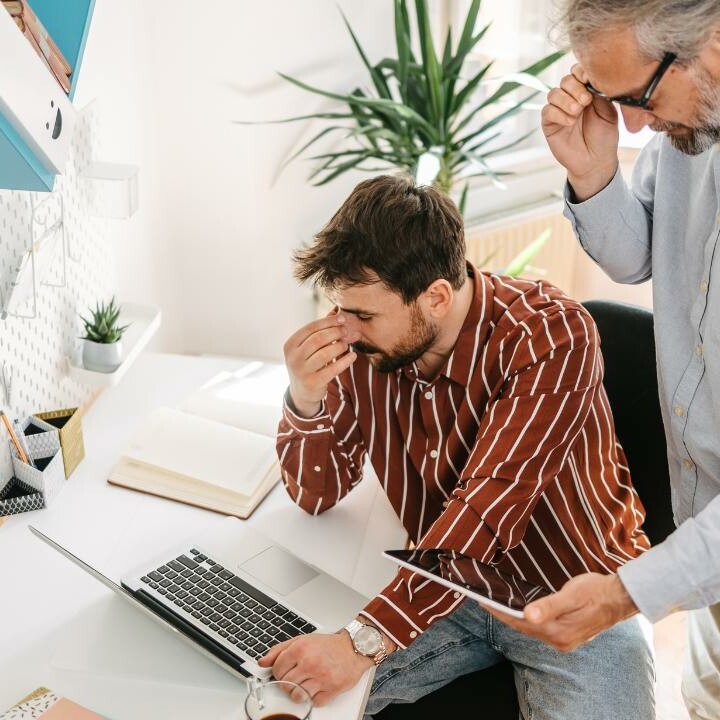 An admin pro being micromanaged by their boss as he sits at the computer and their boss hovers over top.