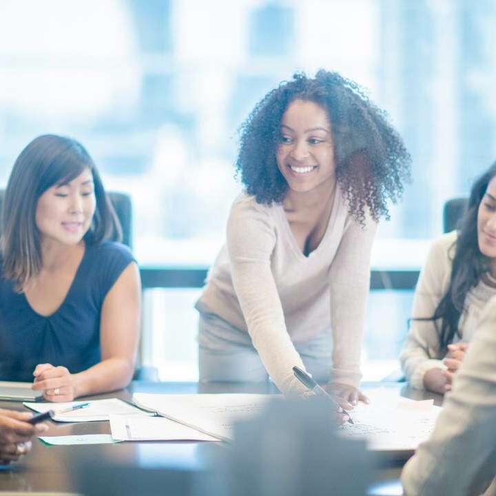 A woman leading a business meeting at a large desk with other employees