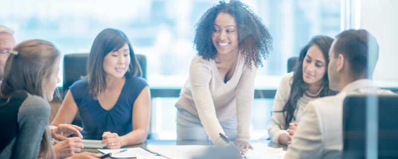 A woman leading a business meeting at a large desk with other employees