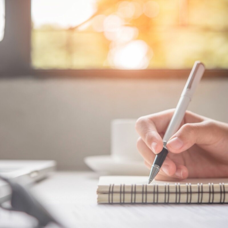person writing shorthand on piece of notepad paper