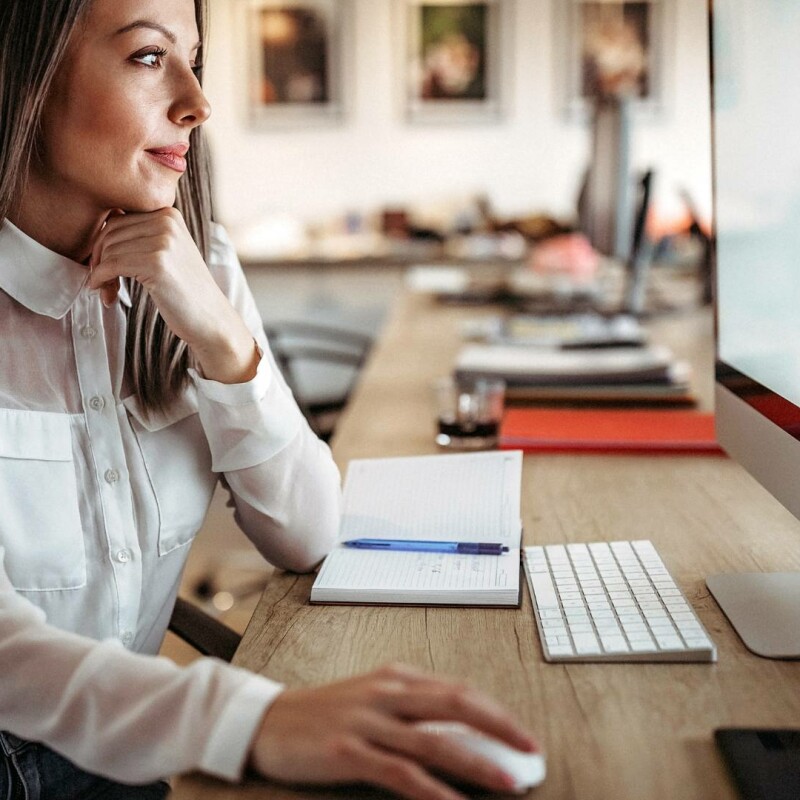 An administrative professional sitting at her computer, using a Canva infographic to enhance her job performance.