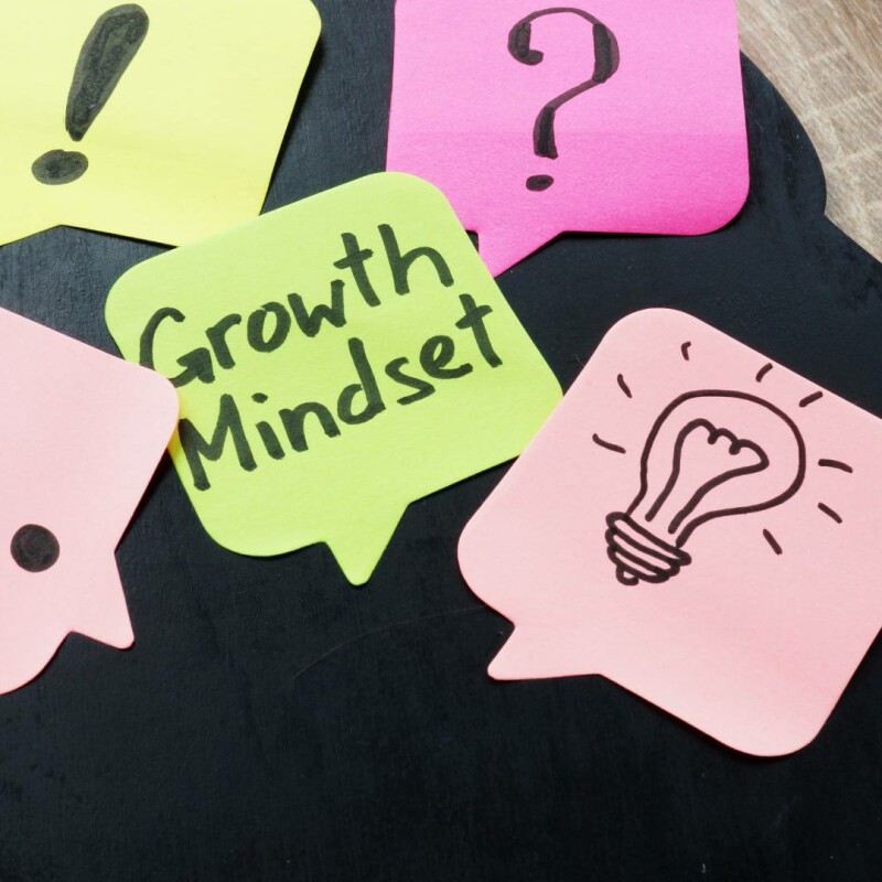 An image of post-it notes, one says growth mindset, and others have a picture of a lightbulb, question mark, and exclamation points. This photo emphasizes the differences between a growth mindset vs fixed mindset.
