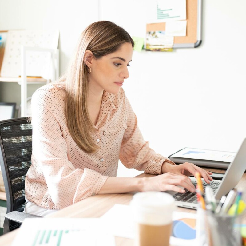 An administrator working hard at her desk on her laptop. She is implementing AI tools her in writing techniques.