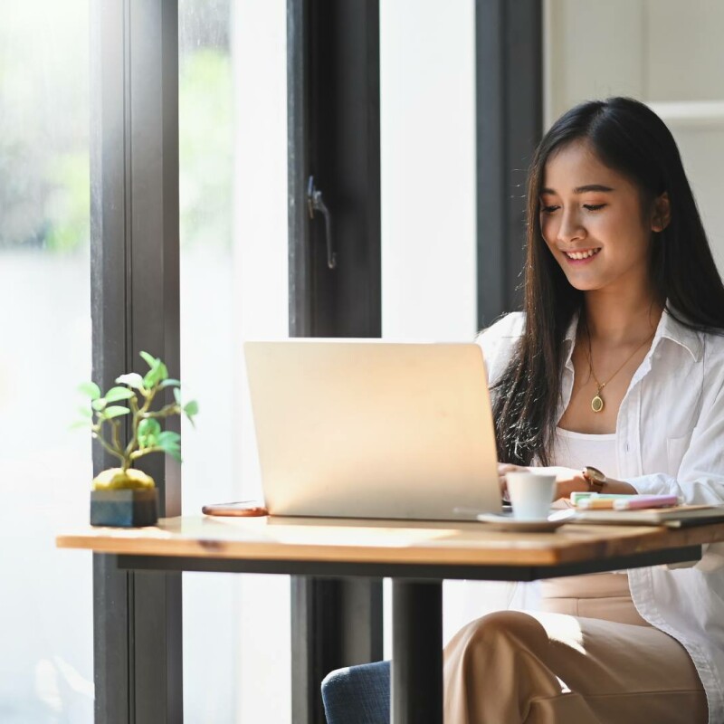 Executive assisting can be challenging at times. This executive assistant is smiling at her desk in front of her laptop. She's made her job seamless thanks to additional tools and technology.