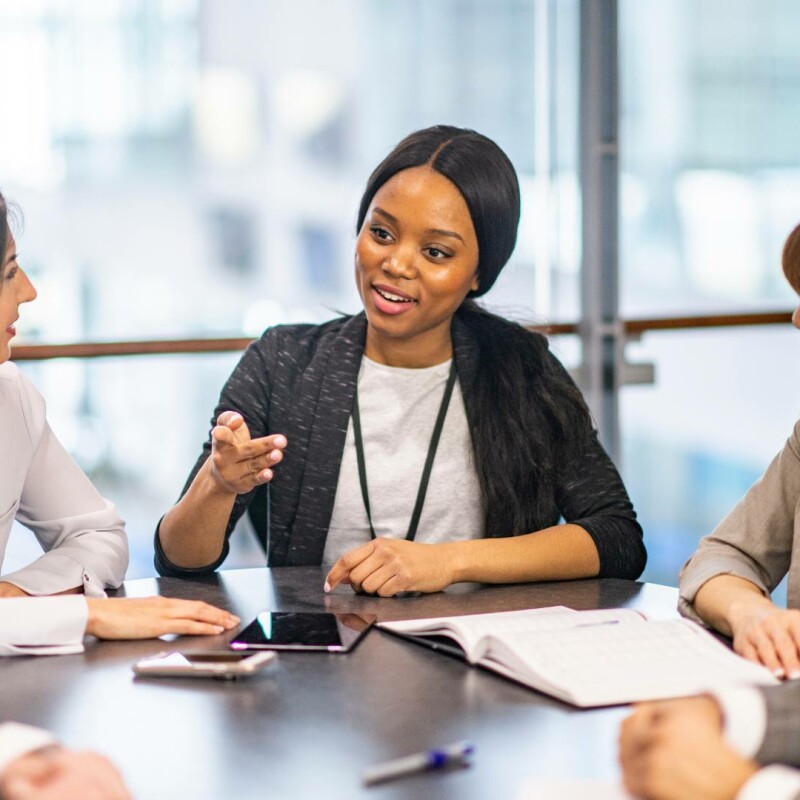 An executive assistant sitting in a boardroom with her executives. She is exuding confidence and speaking with clarity.