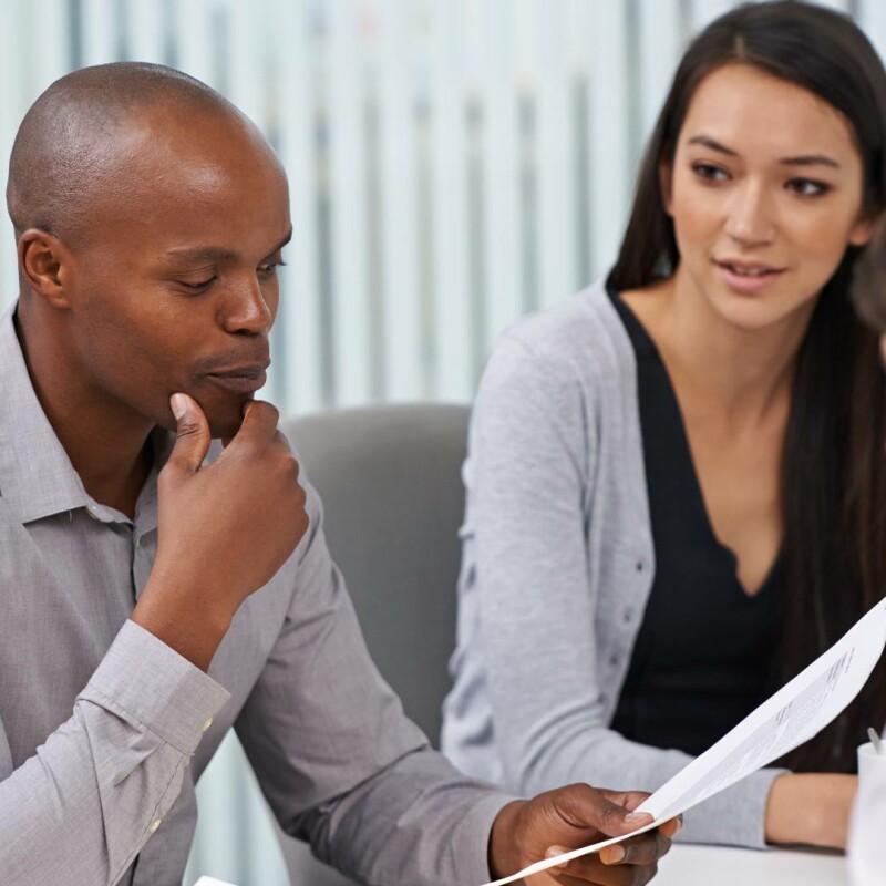 A group of professionals gathered around a meeting table. One man is practicing being decisive, ensuring his workplace remains efficient and productive.