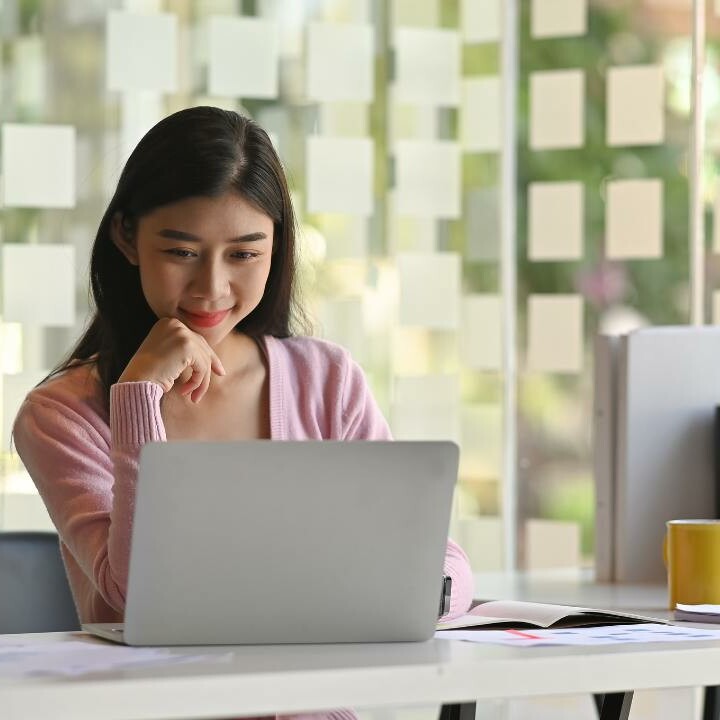 An administrative professional reads on her work laptop about word tips to use in the workplace.