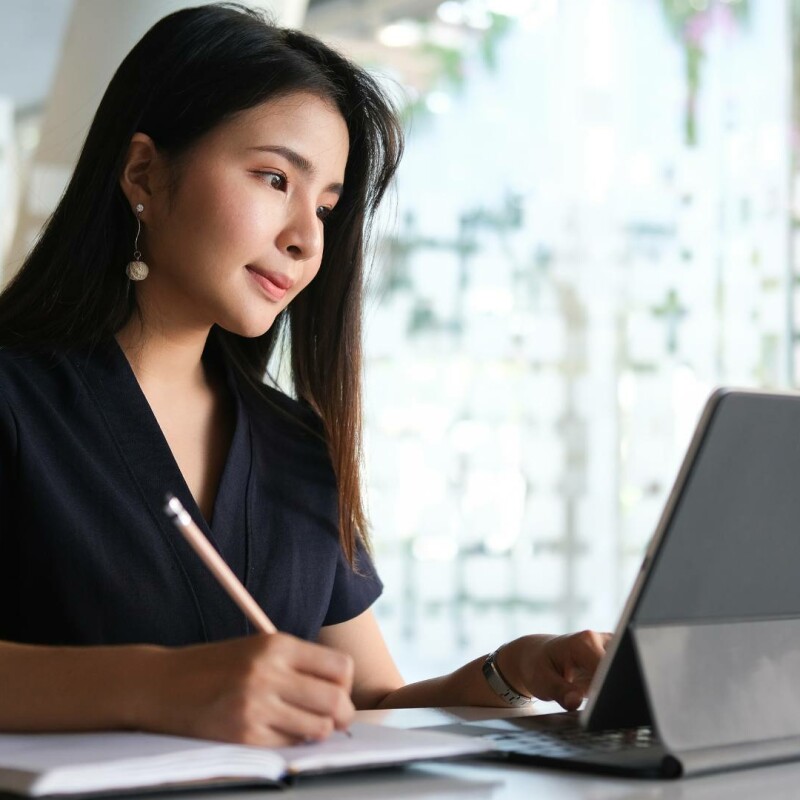 An administrative assistant sits at a desk and works on a standard operating procedure template on a laptop.