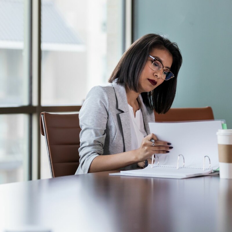A woman sits at a conference table, looking through her binder of important information. Image demonstrates how administrative assistants grow.