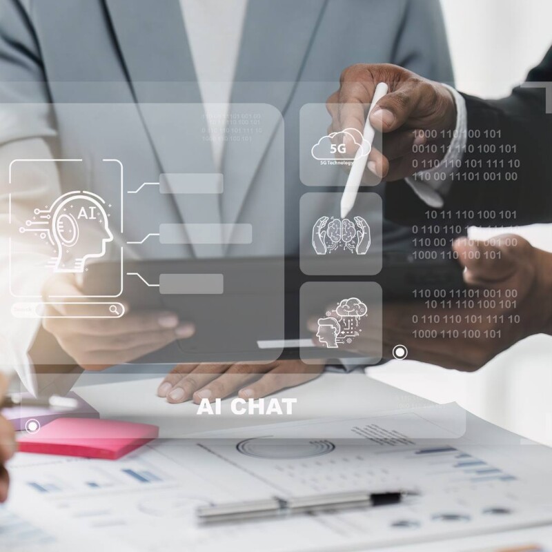 Two employees stand at a desk and review AI technology.