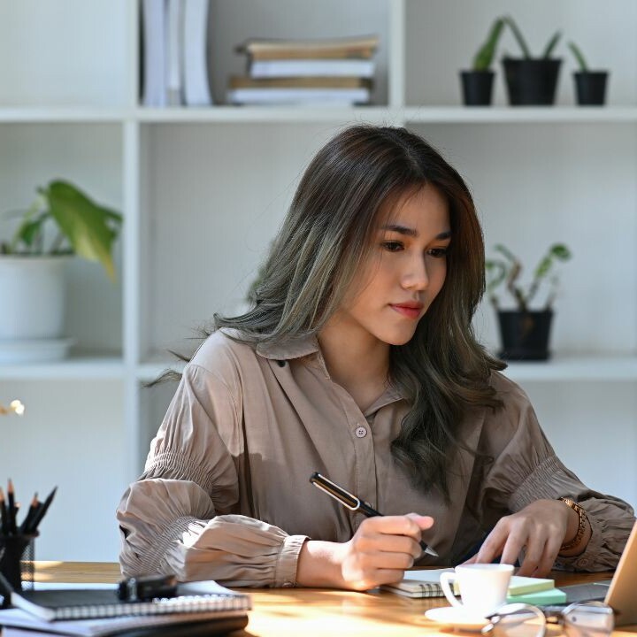assistant sitting at desk, writing notes and looking at laptop