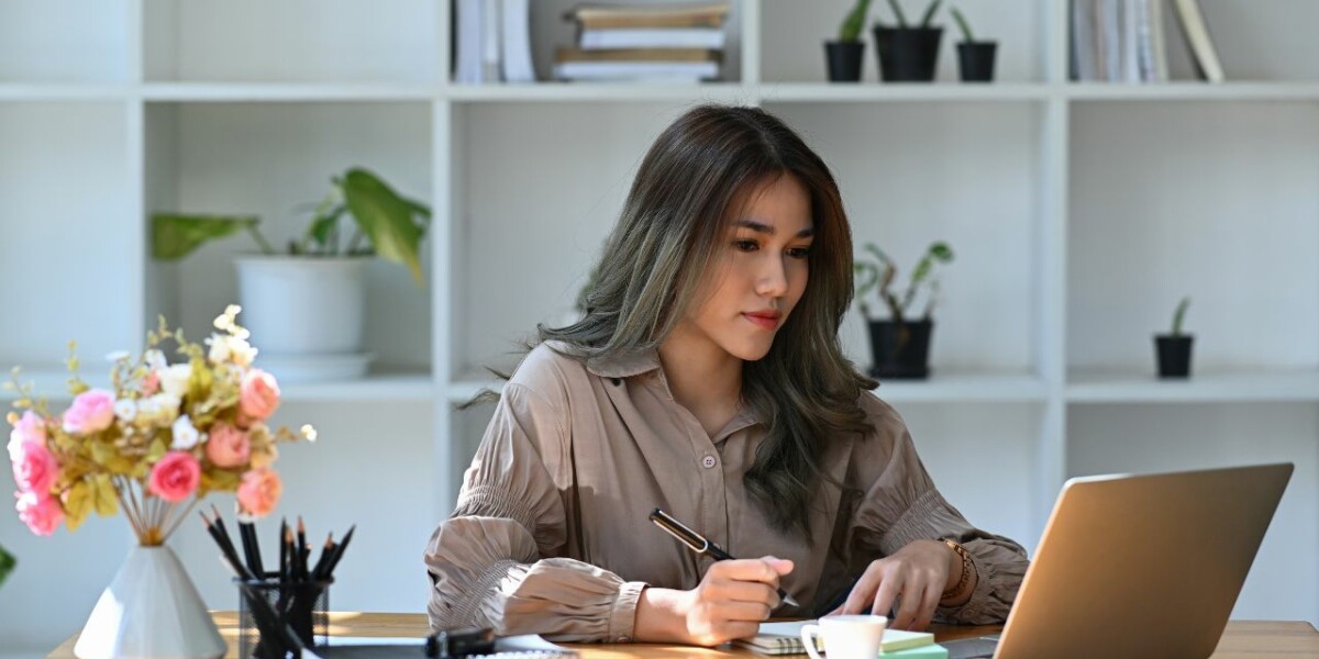 assistant sitting at desk, writing notes and looking at laptop