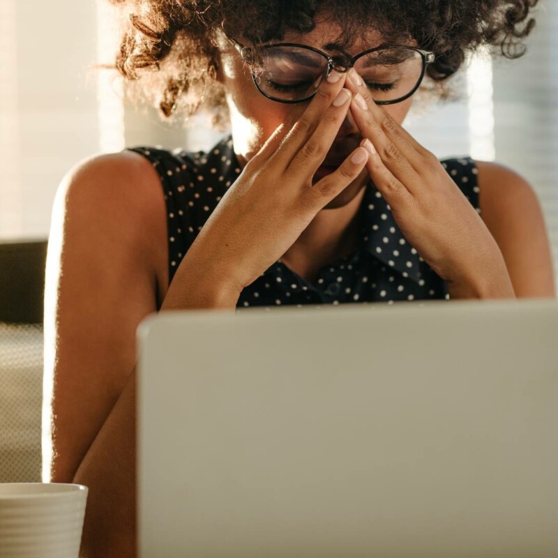 A women sits at her desk in front of her laptop and holds her head in her hands, demonstrating her feeling of burnout.