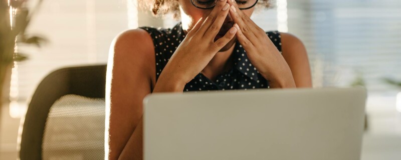 A women sits at her desk in front of her laptop and holds her head in her hands, demonstrating her feeling of burnout.