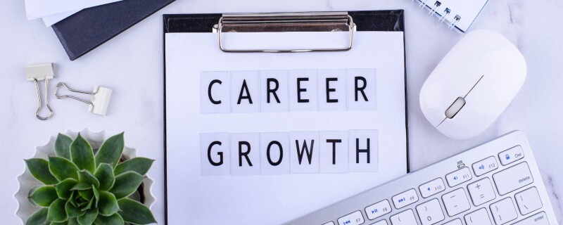 A clipboard with the words "career growth" on it is displayed on a desk surrounded by a keyboard, mouse, and green plant.