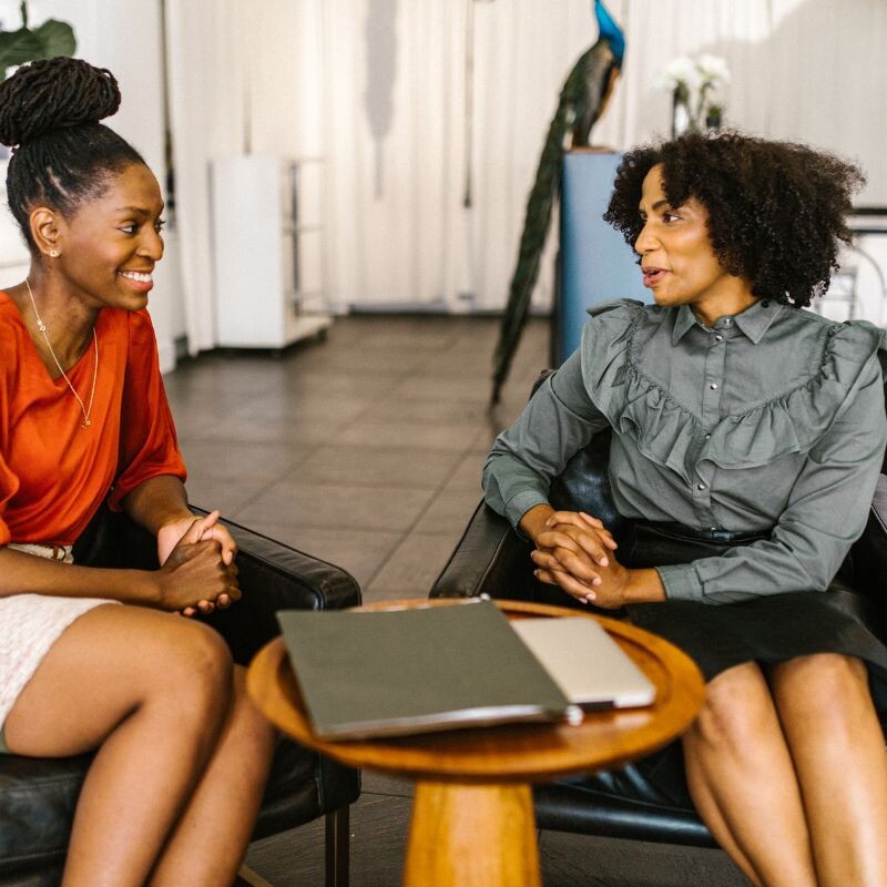Two colleagues, engaged in a focused conversation, with one actively listening and the other speaking.