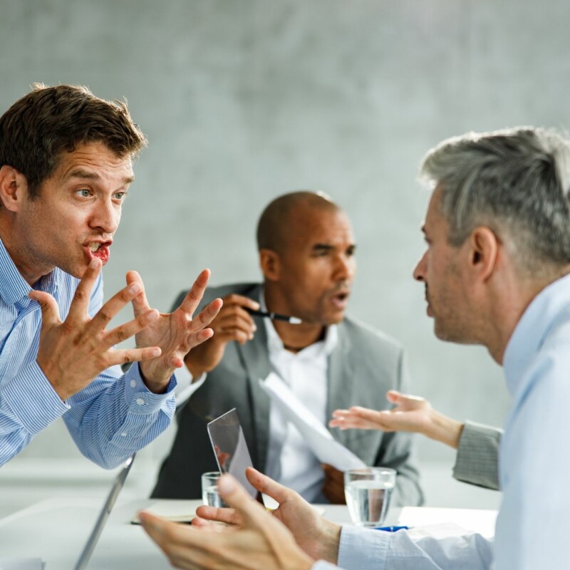 A group of coworkers sitting at a table are arguing due to communication problems in the workplace.