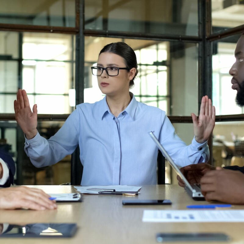 A woman practices conflict resolution skills with her coworkers, putting herself between the two to mediate.