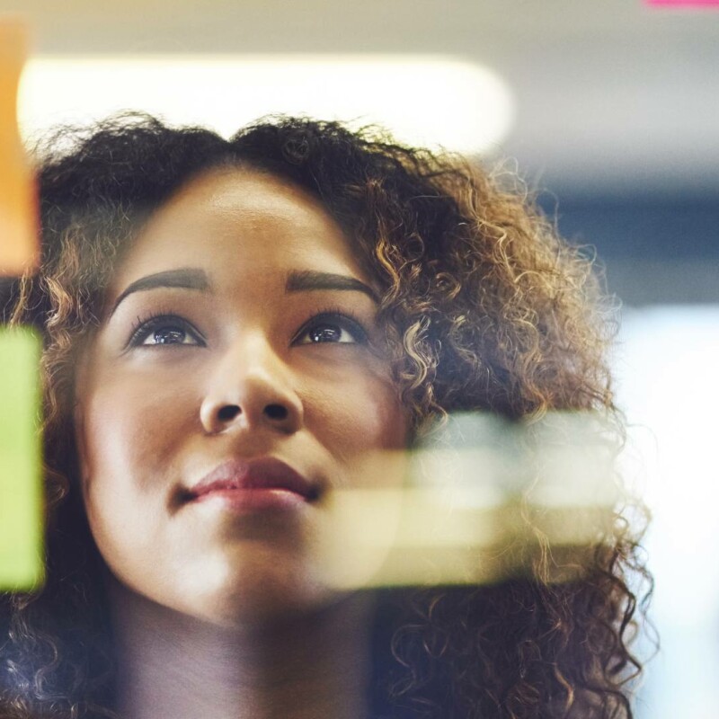 A women looks at post-it notes on a work board, demonstrating critical thinking skills.