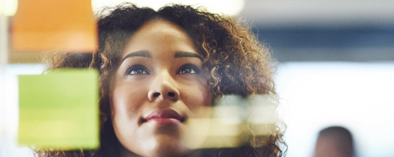 A women looks at post-it notes on a work board, demonstrating critical thinking skills.