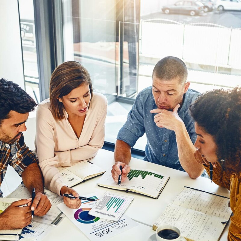 Four employees sit around an office table and work on data tracking and analysis.