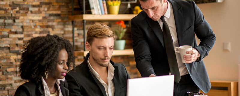 Three coworkers sit together behind a computer, working together on their data management system.
