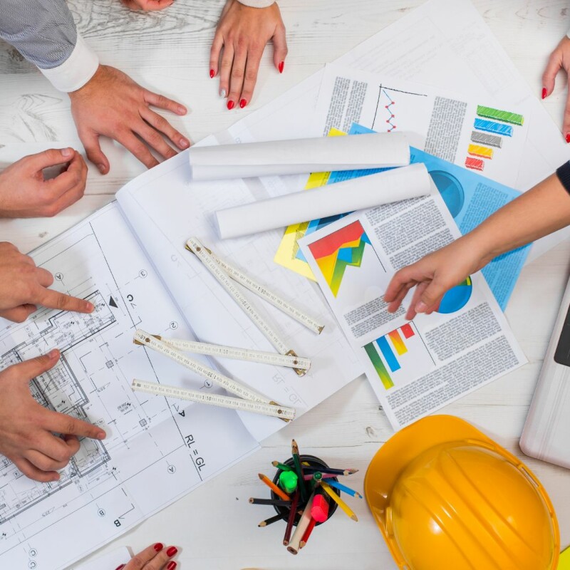 A group of team members are looking down at graphs, documents, and plans together. Image demonstrates importance of strong decision-making.
