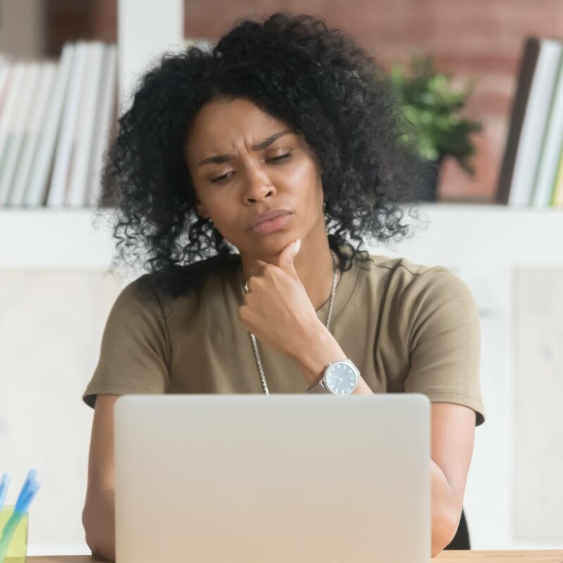 A woman sits at her desk looks at her laptop with a contemplative look on her face. She is demonstrating being decisive.