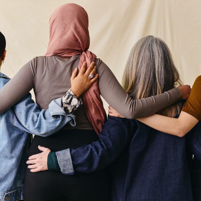 A group of four employee stands together with their backs facing the camera, demonstrating diversity and inclusion in the workplace.