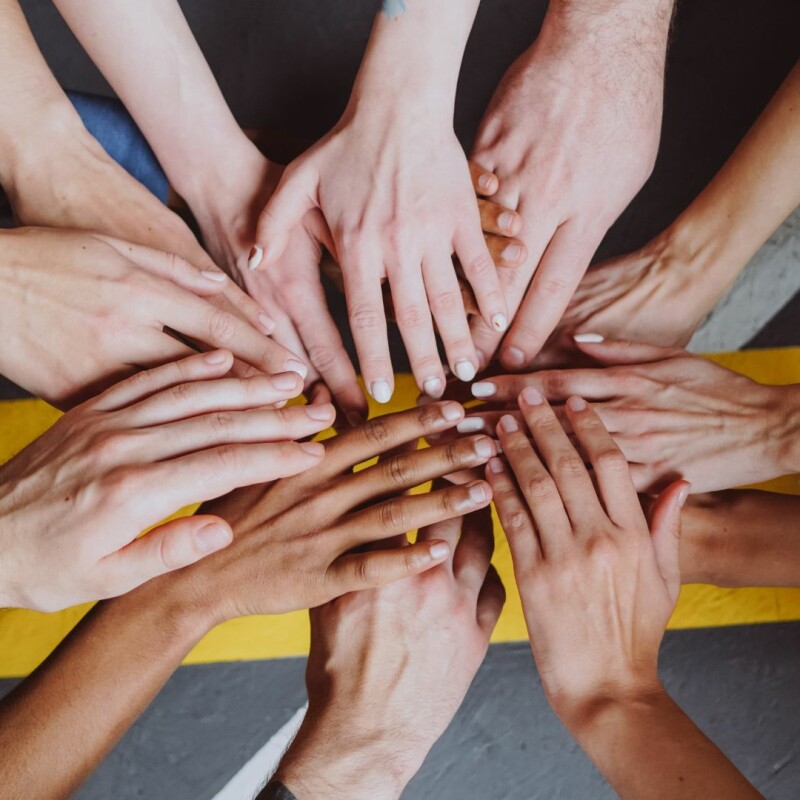 A group of hands belonging to people of all different races meet in the middle, representing diversity and inclusion.