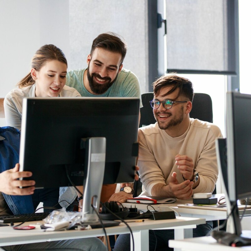 A group of coworkers sit at the same computer while on their coworkers explains something on his screen. Image demonstrates the importance of employee training.