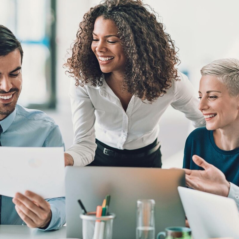 Two men and two women gather around a desk. They are creating an effective executive brand while looking at paperwork and a laptop together.