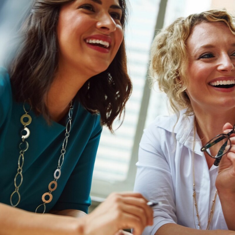 Two coworkers smile, working hard to earn their holiday bonus.