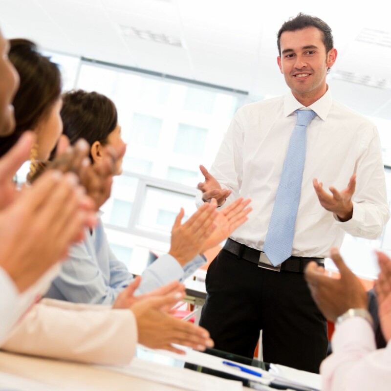 A team works together, looking up from their table up at a coworker. Image demonstrates importance of learning how to be flexible at work.