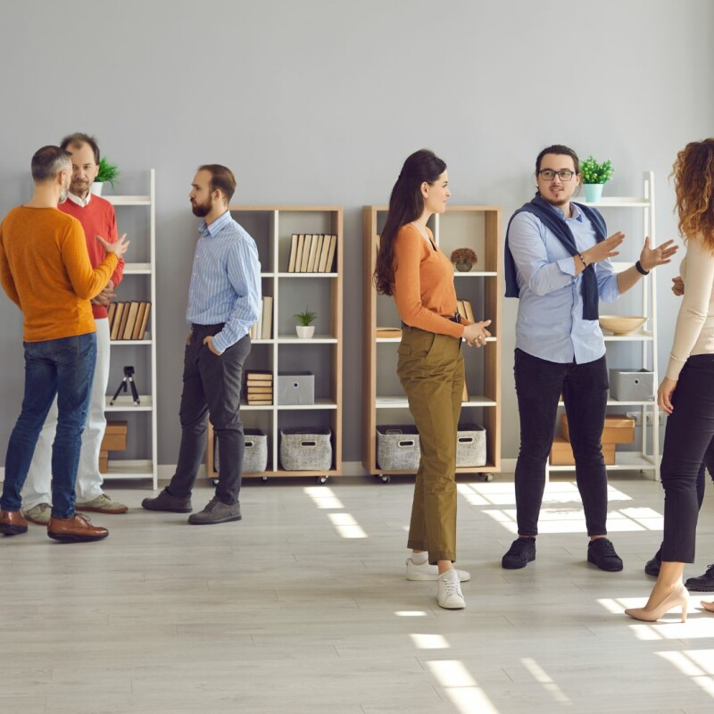 A large group of coworkers are split off into two groups, talking and working together. Image demonstrates importance of interpersonal skills.