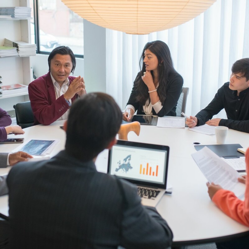 A group of coworkers sit around a table, all of their attention on their manager.