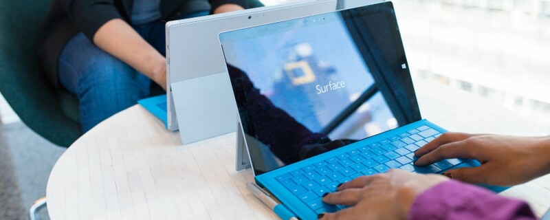 Two coworkers sit across from each other on a table, working on Microsoft Tablets. Image demonstrates how Microsoft OneDrive can be used collaboratively.
