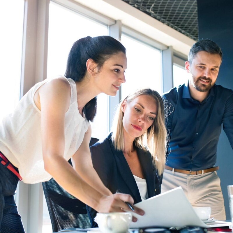 Three people sit at a computer and work with efficiency, demonstrating the skills of an office manager.