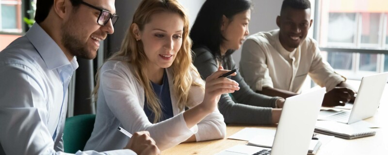 Four employees sit in groups of two and look at computer data to choose the right payment software.