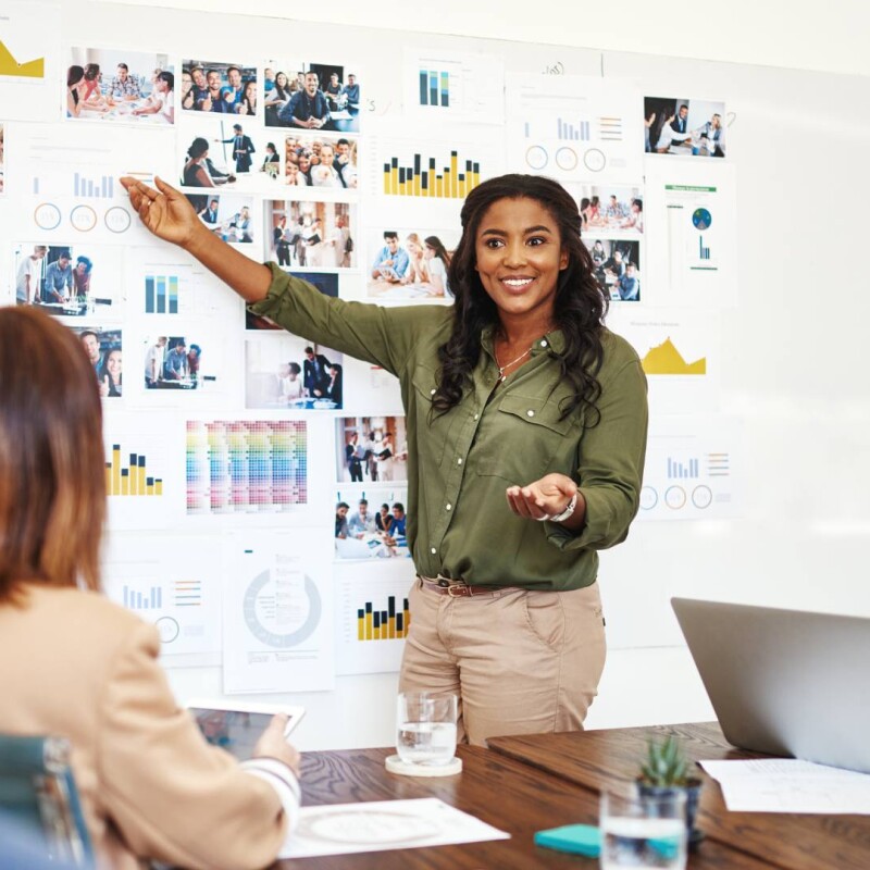 A senior-level executive stands at the front of the room speaking to three employees, demonstrating strong people management skills.