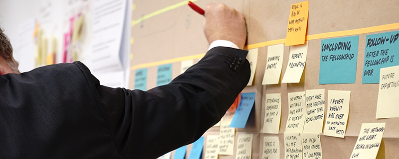 person in suit writing on a board with post-it notes