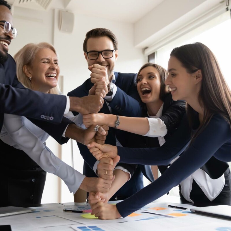 A group of coworkers gathers today, smiling and laughing, demonstrating successful relationship building.