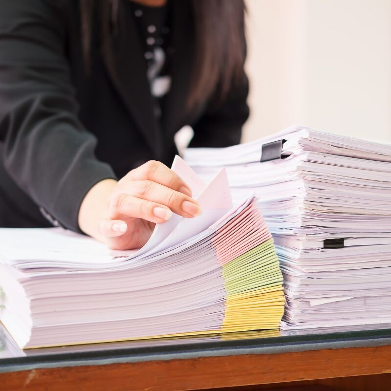 Legal secretary managing multiple complex legal documents at a desk.