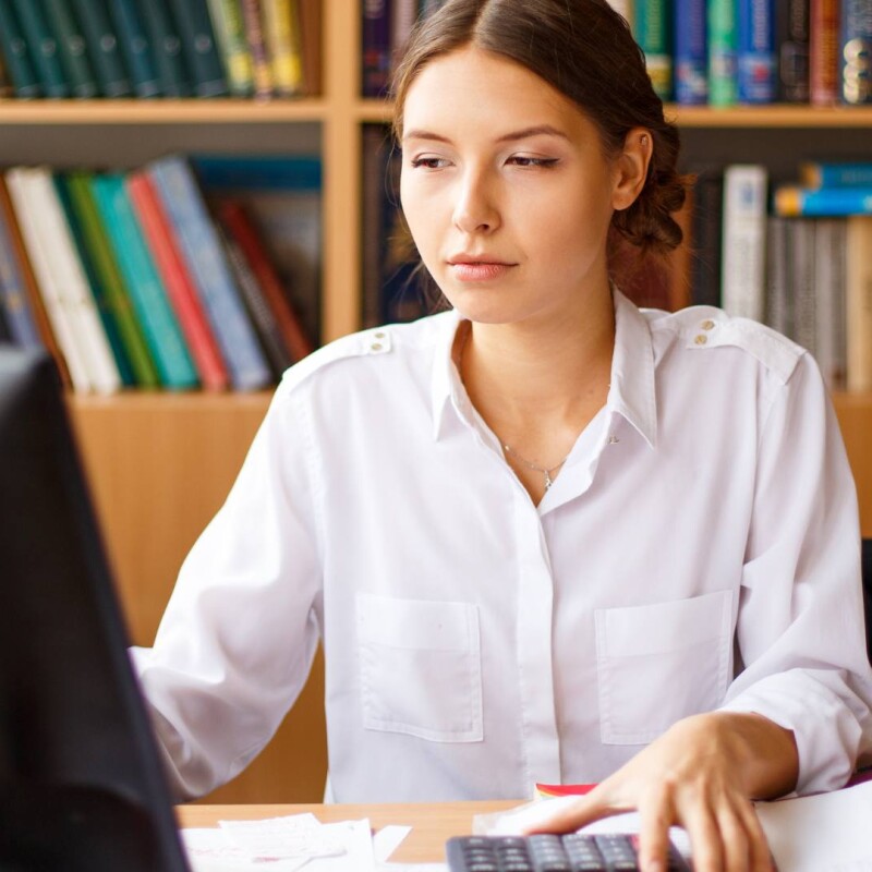 An administrative professional sits at her desk and uses the computer, demonstrating software solutions for admins.