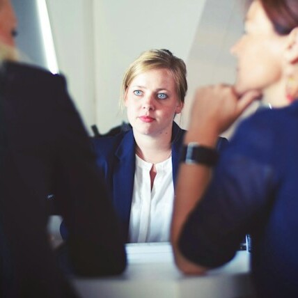 An executive assistant sits at a table and is being interviewed by two managers, demonstrating a job interview