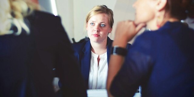 An executive assistant sits at a table and is being interviewed by two managers, demonstrating a job interview