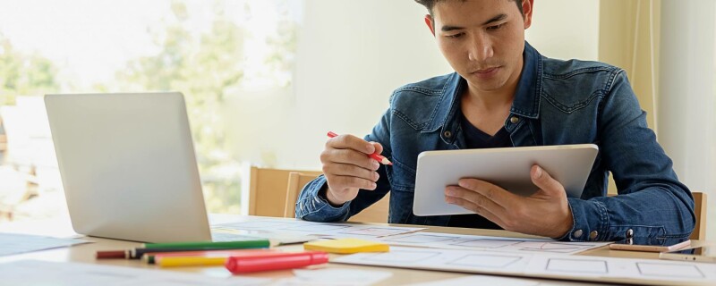 A person sits at a desk with a laptop, tablet, paperwork, and writing utensils. They are working on a vendor management template.